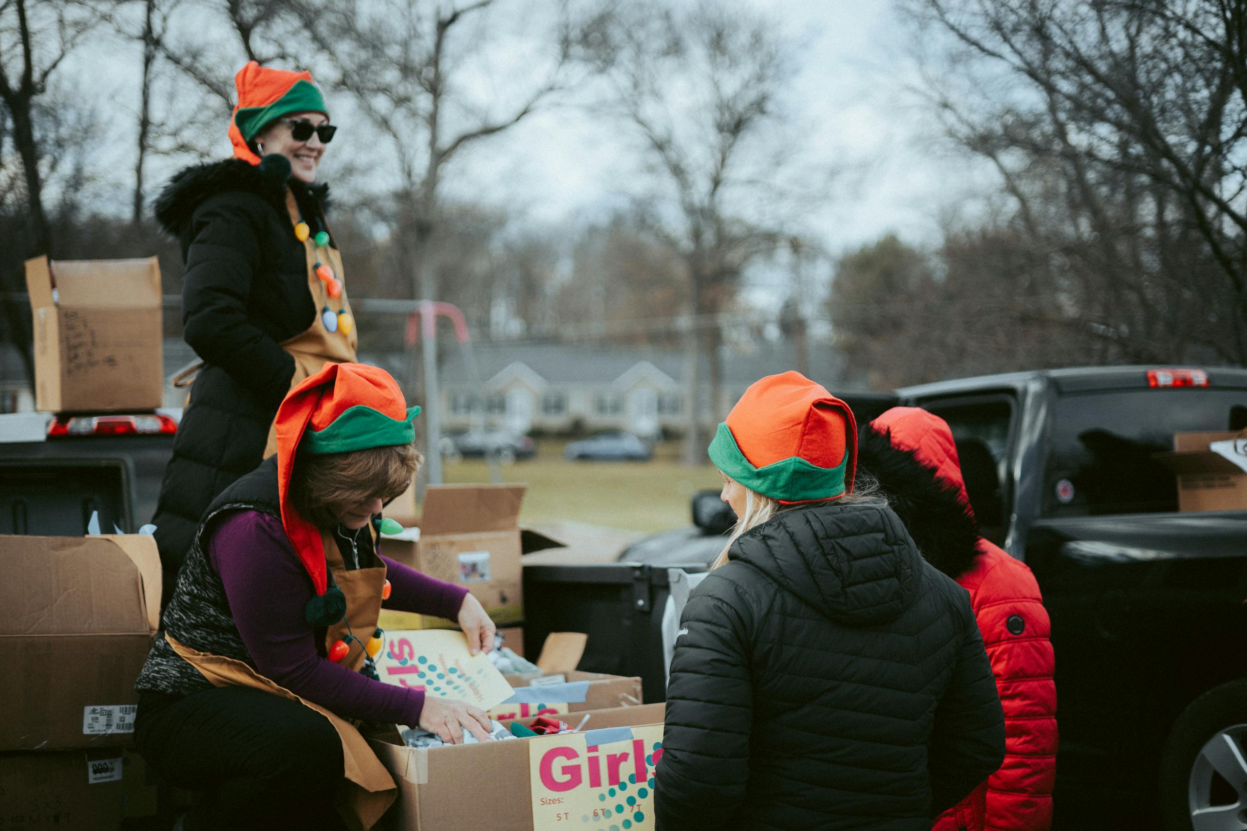 A group of volunteers in festive attire distributing Christmas gifts from truck.