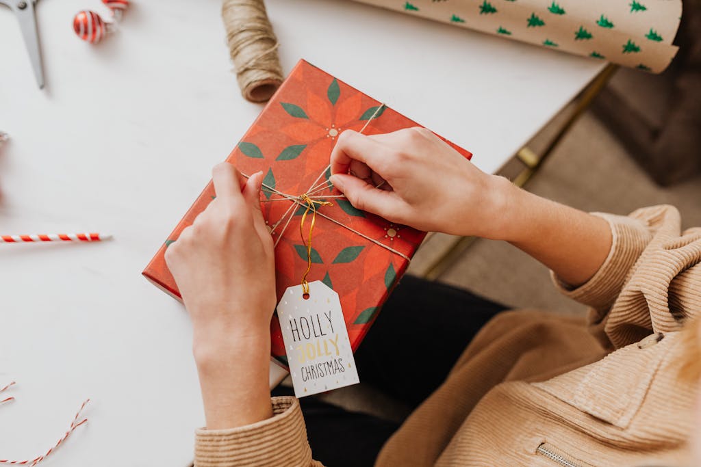 Hands wrapping a red Christmas gift with a 'Holly Jolly' tag, adding festive cheer.