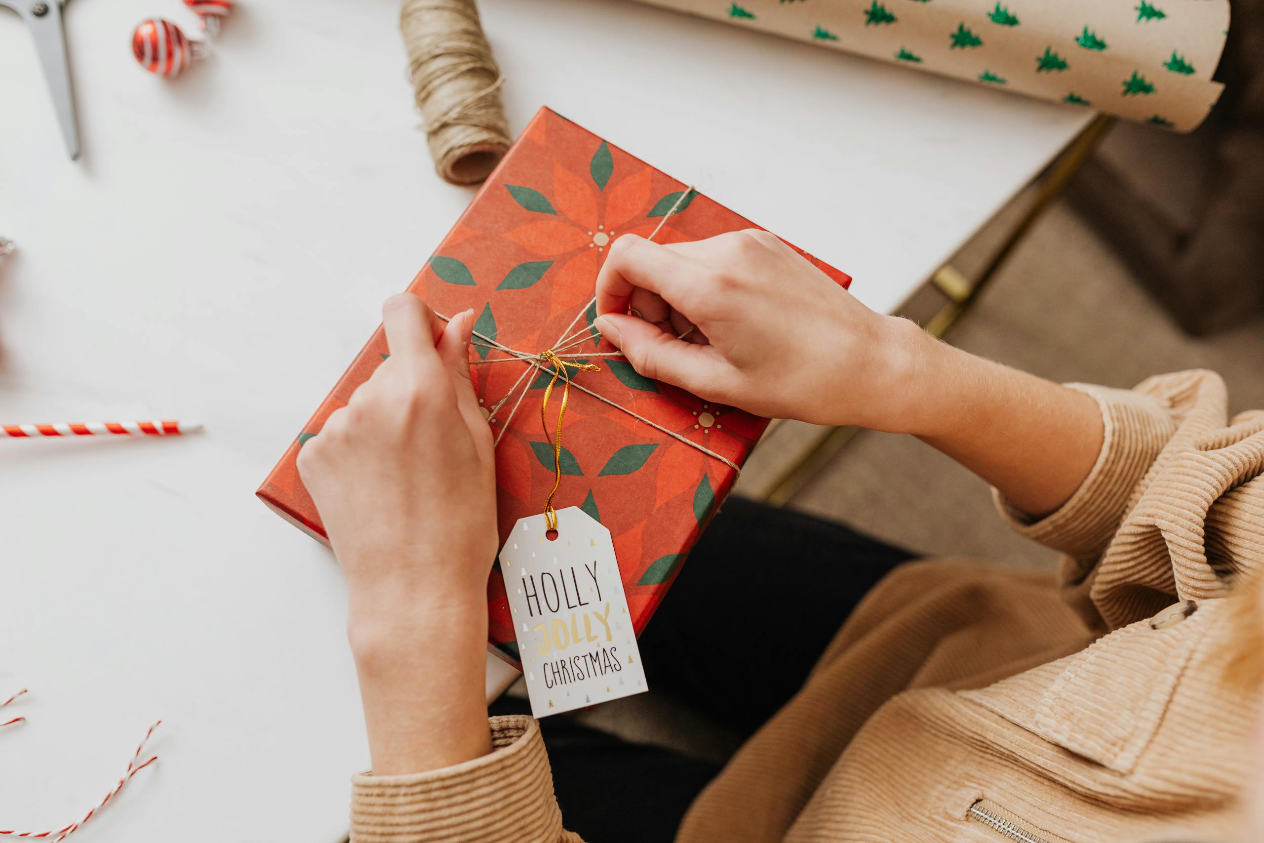 Hands wrapping a red Christmas gift with a 'Holly Jolly' tag, adding festive cheer.