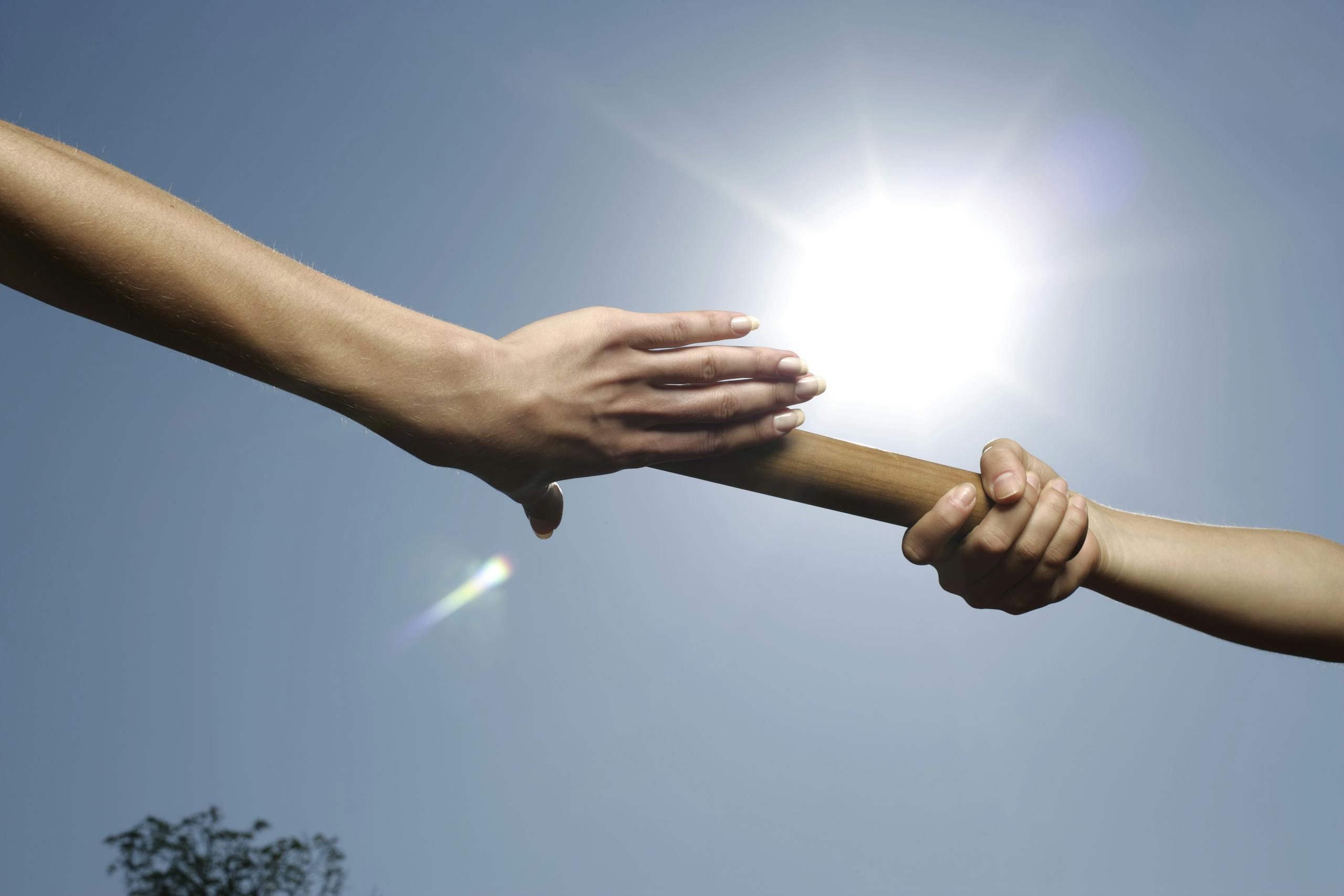 Two hands passing a baton under a bright sun, symbolizing teamwork and cooperation.